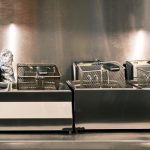 A deep fryer sits in front of a stylish stainless steel wall in a commercial kitchen.