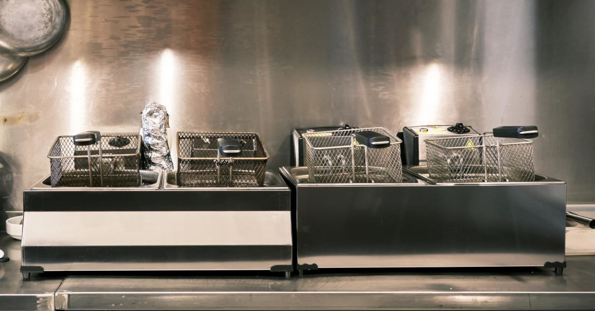 A deep fryer sits in front of a stylish stainless steel wall in a commercial kitchen.