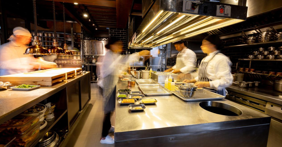 Chefs work under the bright lights of a busy commercial kitchen.
