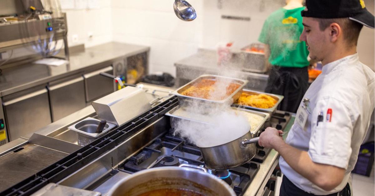 A chef prepares hot dishes in a commercial kitchen.